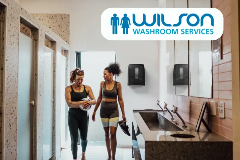 Two women in clean washroom with North Shore hand towel dispenser on wall